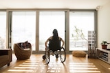 An unidentifiable woman in a wheelchair at home on her own.