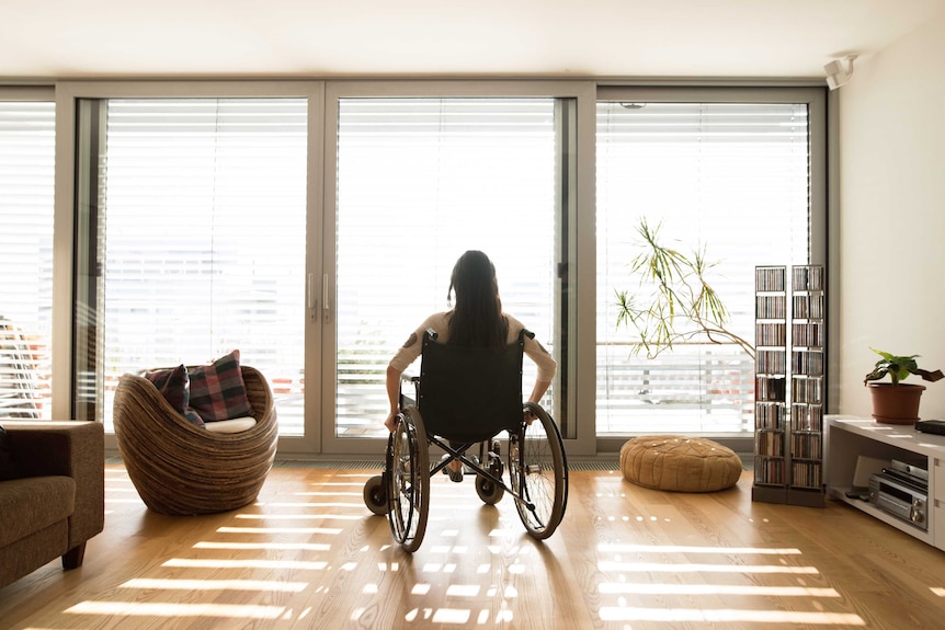 An unidentifiable woman in a wheelchair at home on her own.