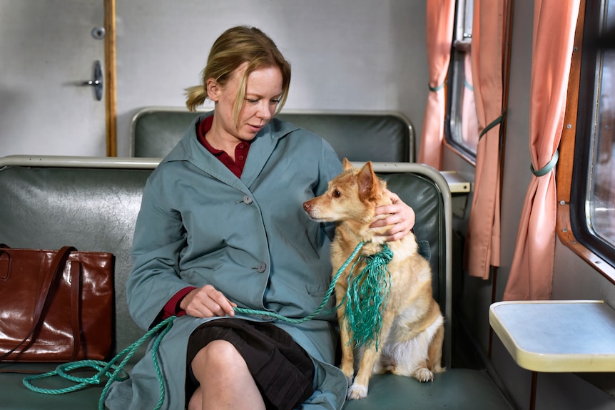 A film still of Alma Pöysti sitting on an old-fashioned train in a coat, with her arm around her dog.