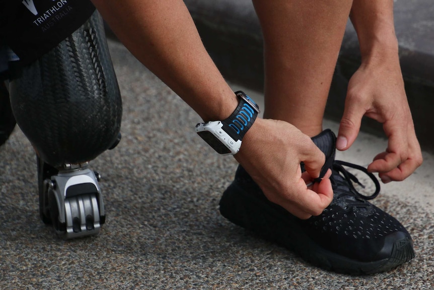 A close-up shot of a man with a prosthetic leg tying his shoelace.