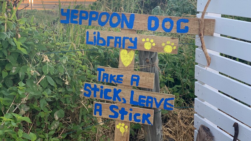 A sign at the beach advertising a 'dob library' with a pile of sticks underneath