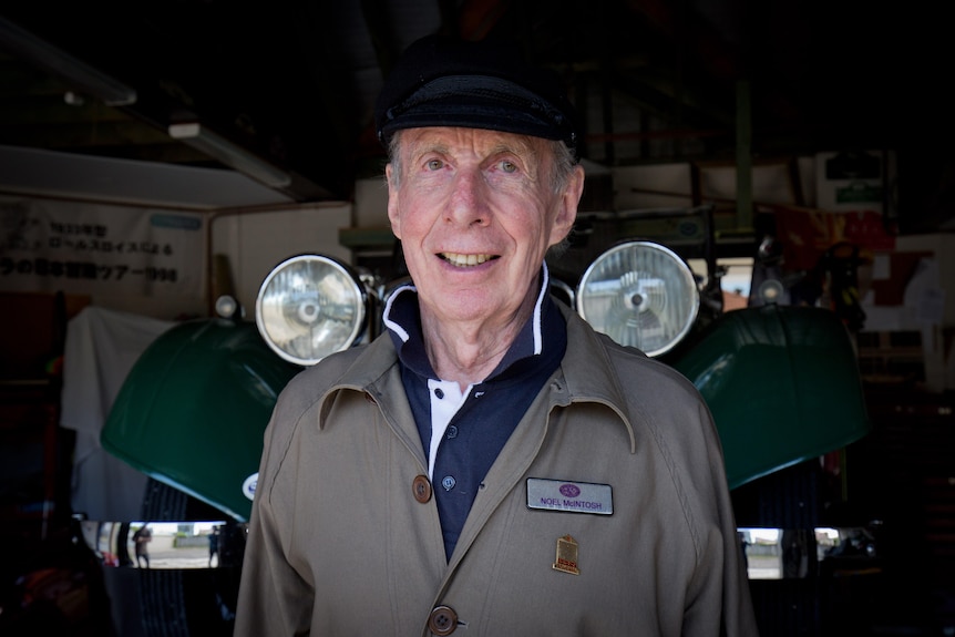 Noel smiling at the camera and standing in front of an old car.