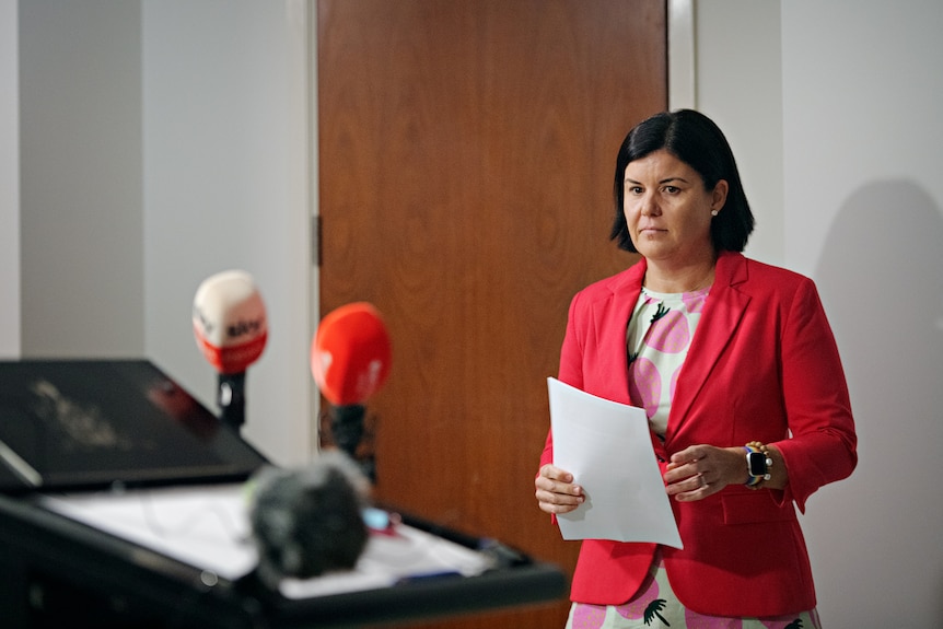 NT Chief Minister Natasha Fyles,  in a bright pink blazer, standing inside a room and looking at a nearby lectern.