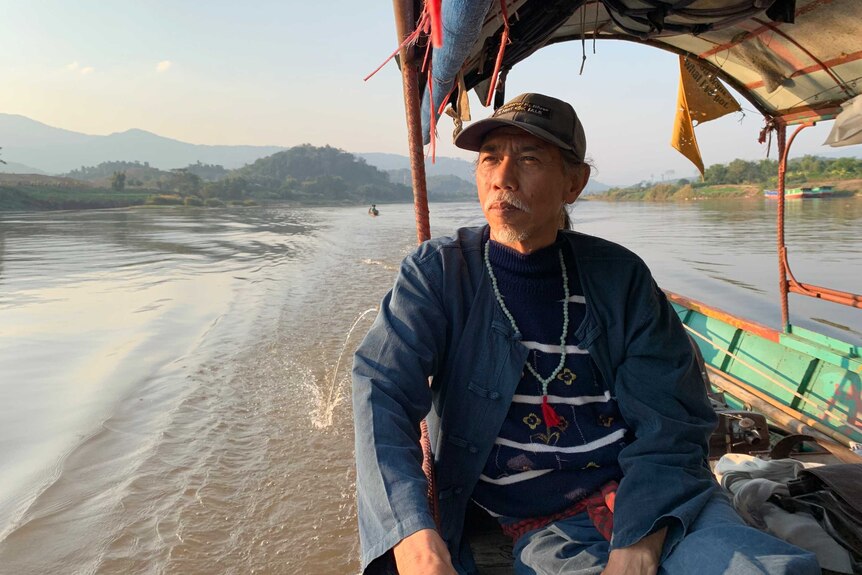 A man looks out to the side as he drives a boat along the Mekong River.