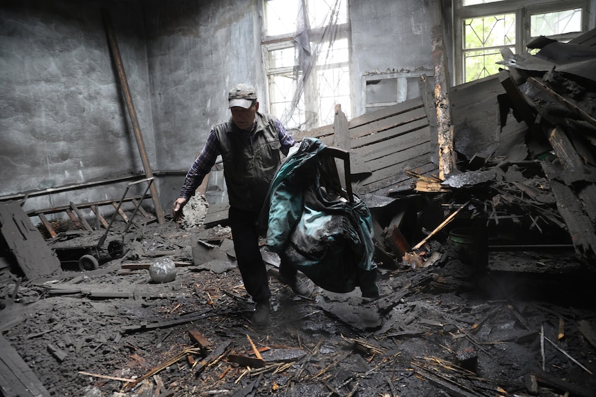Un hombre toma sillas en una casa que fue destruida por el bombardeo.