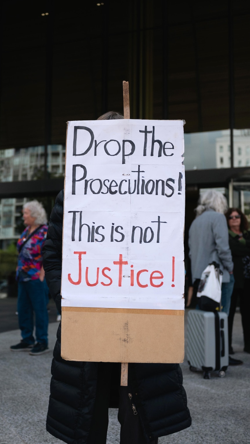 A sign reading 'Drop the Prosecutions! This is not Justice' held be a person outside the ACT Supreme Court.