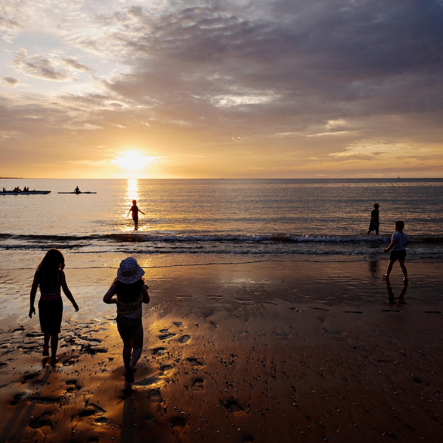Children play on the sand at Mindil Beach as the soon goes down on the horizon.