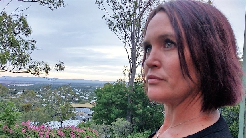 a woman with dark hair stands on her balcony looking off into the distance