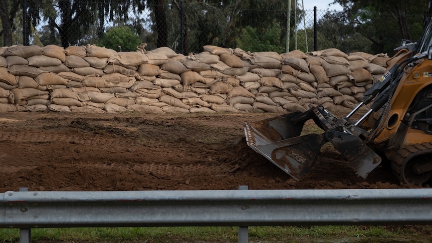 A construction vehicle alongside a road, with sandbags behind it.