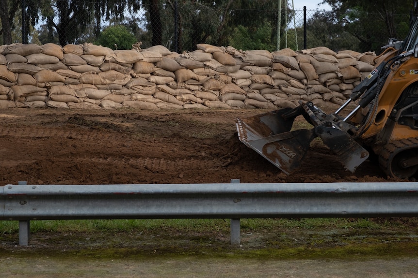 A construction vehicle alongside a road, with sandbags behind it.