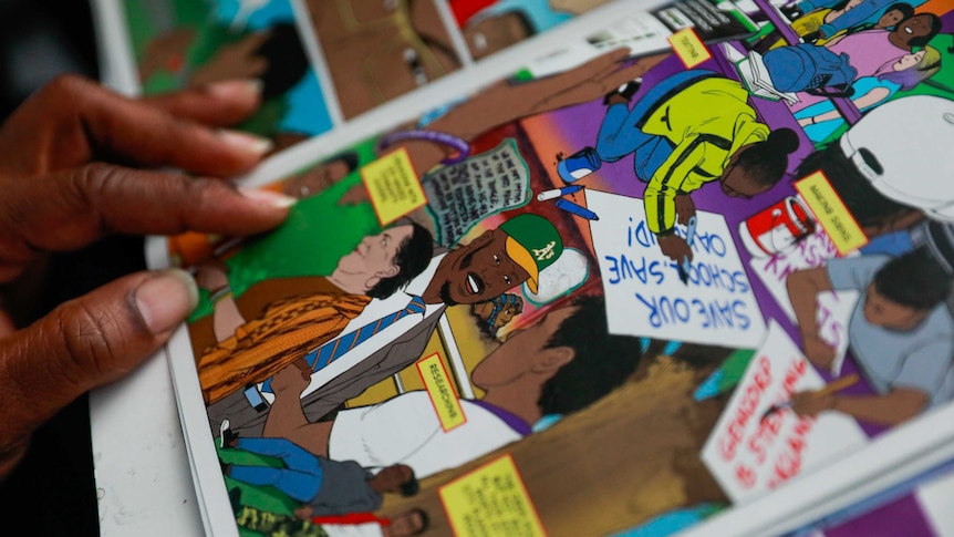 dark skinned man's hand on illustrated book depicting people of diverse backgrounds