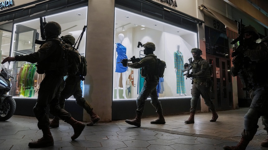 Israeli security forces in uniform with guns drawn search the streets of Tel Aviv for assailants after shooting