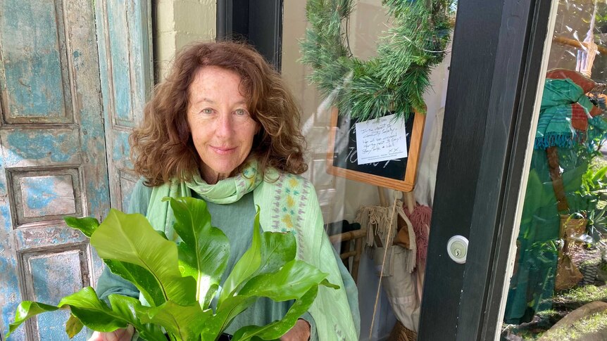 Shop owner Nell Simpson stands with a pot plant outside her store at Palm Beach in Sydney.