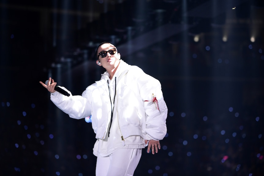 一位穿着白色嘻哈风格服装的中国年轻人在舞台上表演。