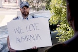 A police officer holds a card that says "We love Australia".