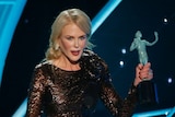 Nicole Kidman hold up her Screen Actors Guild award in front of a blue background.