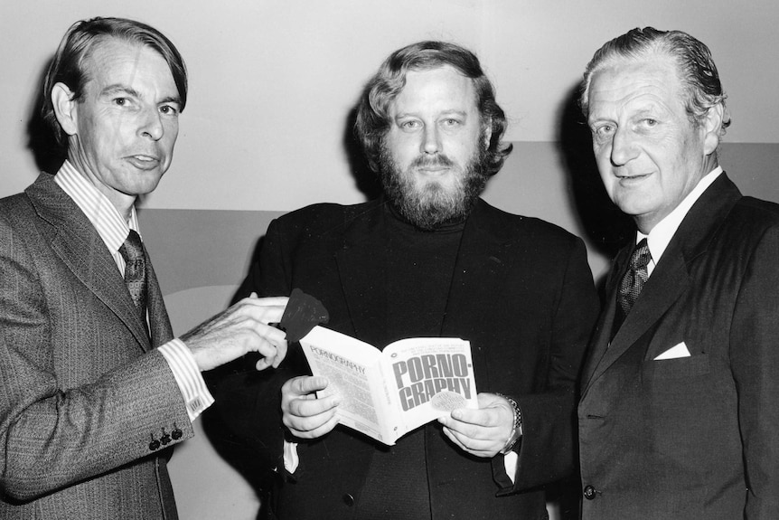 Black and white photo of Adams holding book titled pornography and standing between two men.