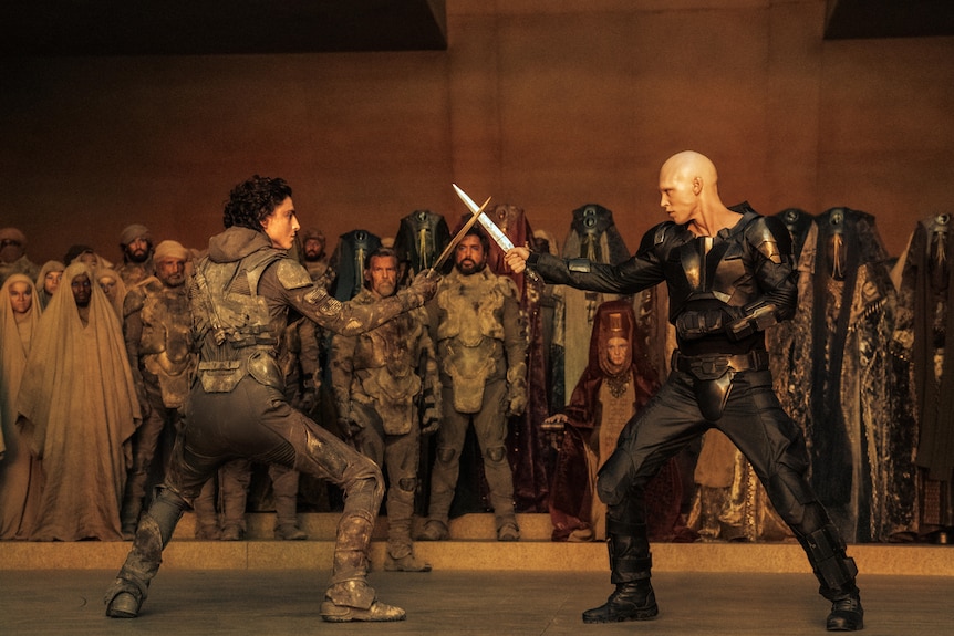 A film still of Timothée Chalamet and Austin Butler fighting with swords, a crowd behind them.