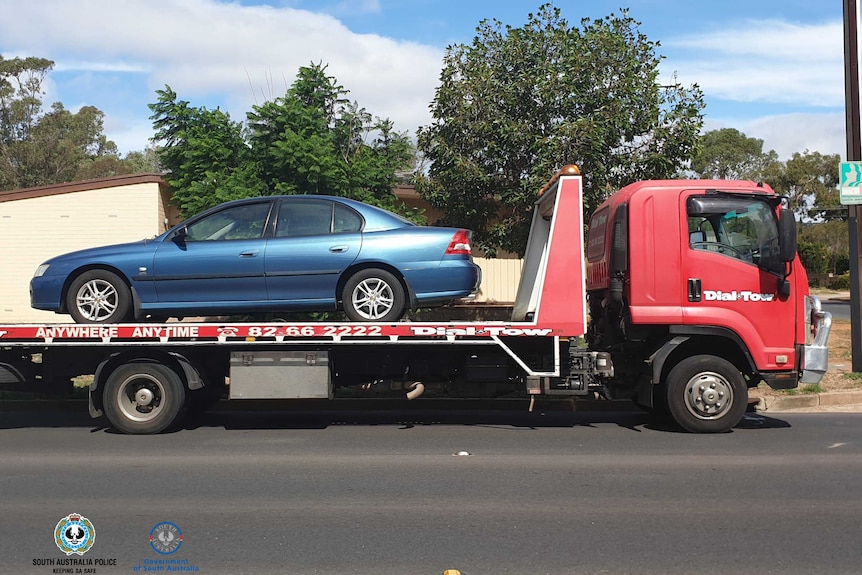 A blue commodore on the back of a red tow truck