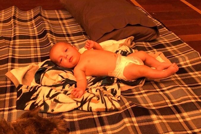 Baby in nappy on rug on the floor.
