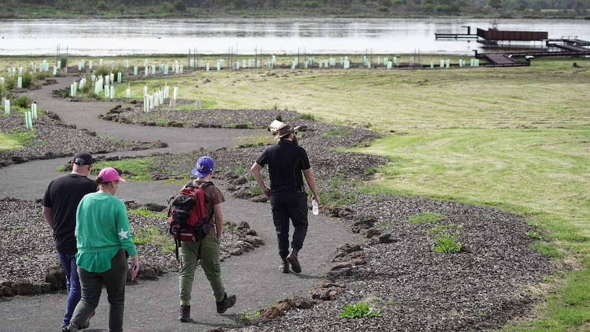 People walk down a path in front of a lake.