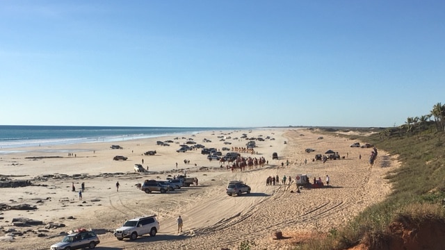 People, cars and camels crowd onto Cable Beach north of the rocks.