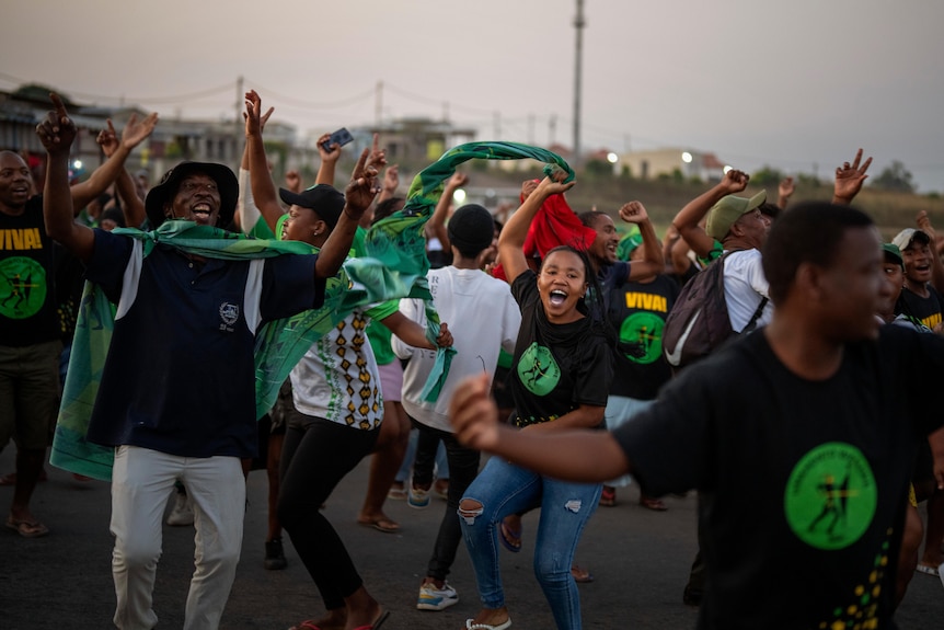 A group of young South African men and women in black and green clothing dance joyously in the street.