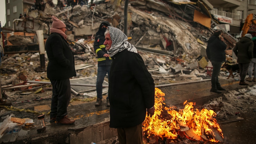 People warm themselves next to a collapsed building in Malatya.