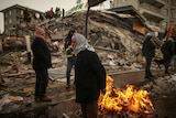 People warm themselves next to a collapsed building in Malatya.