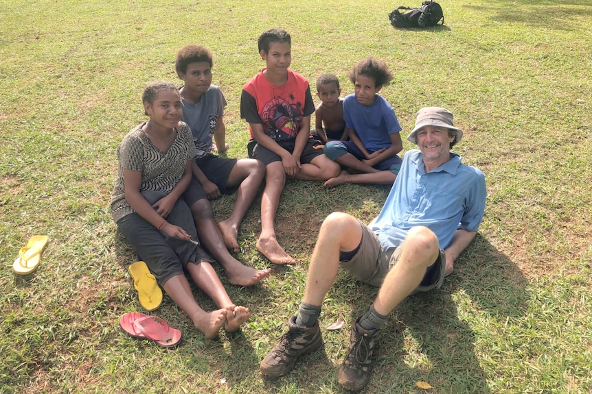 Australian man reclining on ground on right, with five Papua New Guinean teenagers and children sitting with him.