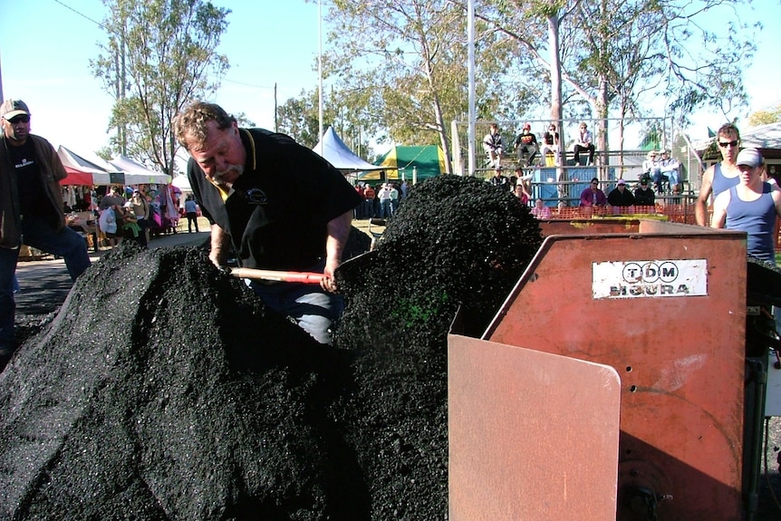 A man stands behind a pile of black coal and shovels it into a bin.