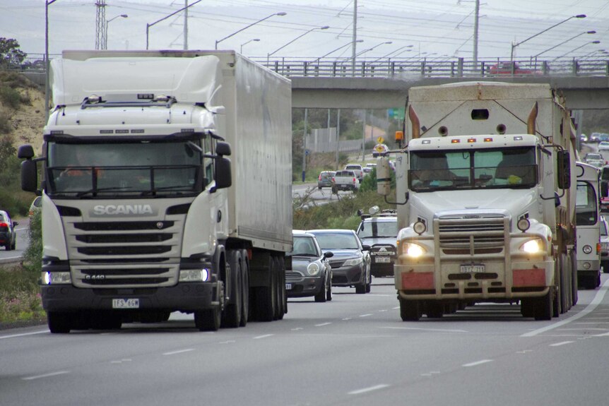 Two heavy haulage trucks travelling along Roe Highway in front of busy traffic.
