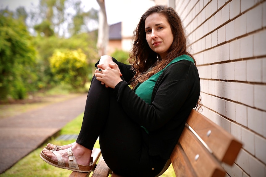 Adriane White sits on a park bench, with her knees to her chest