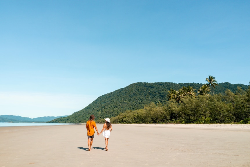 A couple walk along a stretch of beach