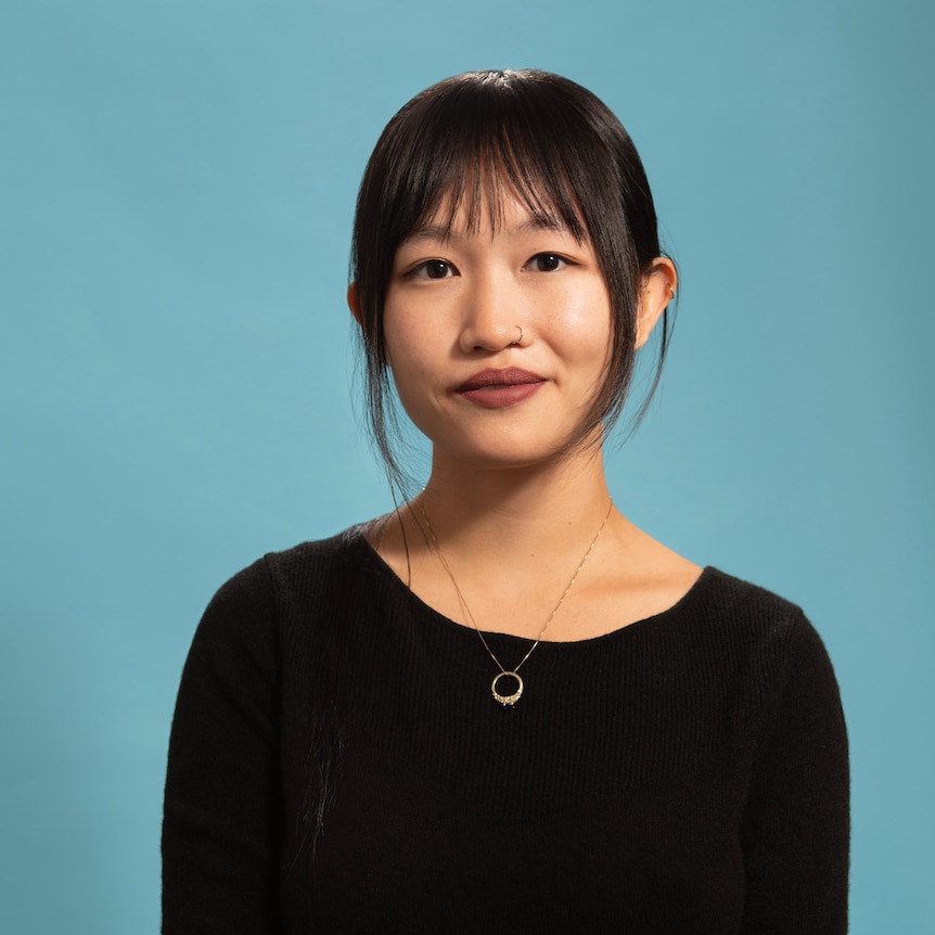 Rebecca F. Kuang with hair tied back, black top, pleated skirt, set against a blue background