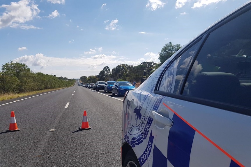 Side of police car on a road closure with cones on road