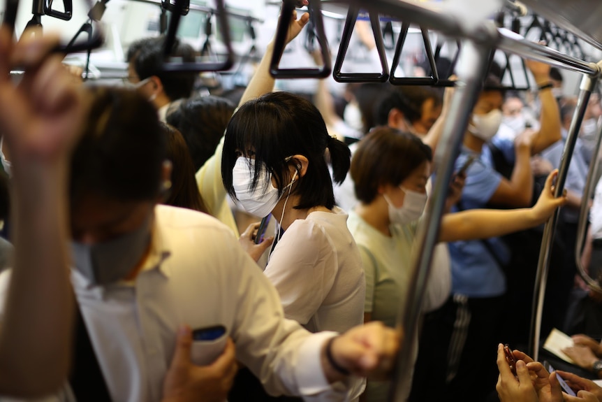 Masked commuters mill around in a train in Tokyo, Japan, August 2021.