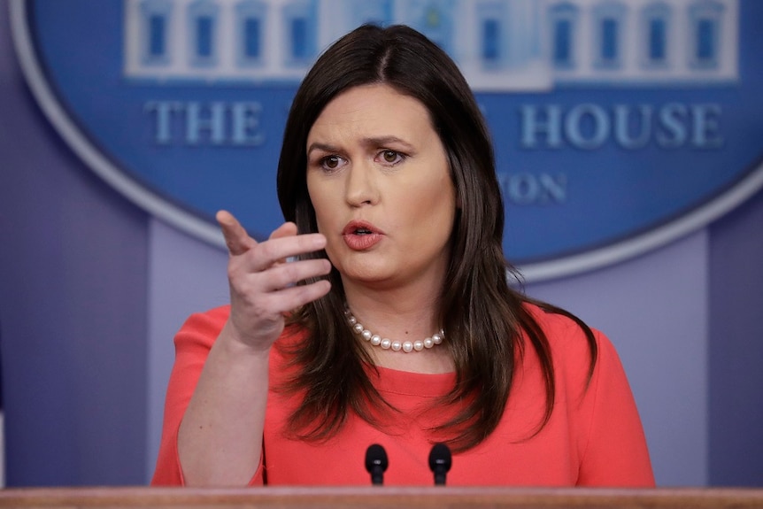 A woman points as she speaks from behind a lecturn