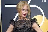 Nicole Kidman poses on the red carpet wearing a black dress in front of a Golden Globes sign.