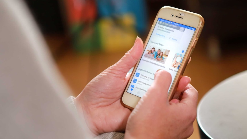 A mobile phone in a woman's wands, with the HealthEngine app open.