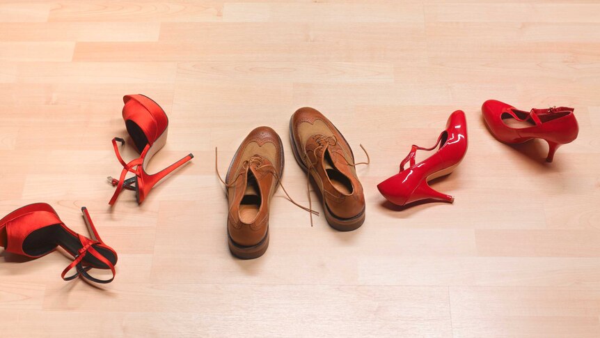 three pair of shoes on the floor, red satin stilettos, men's brogues and red patent leather high heels