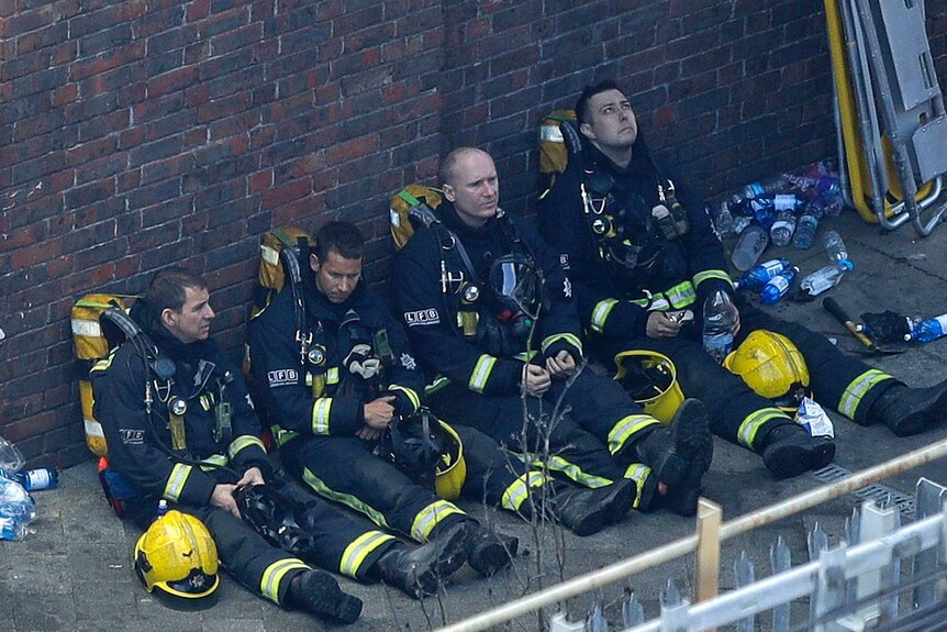 Four firefighters rest against a wall after fighting Grenfell Tower blaze