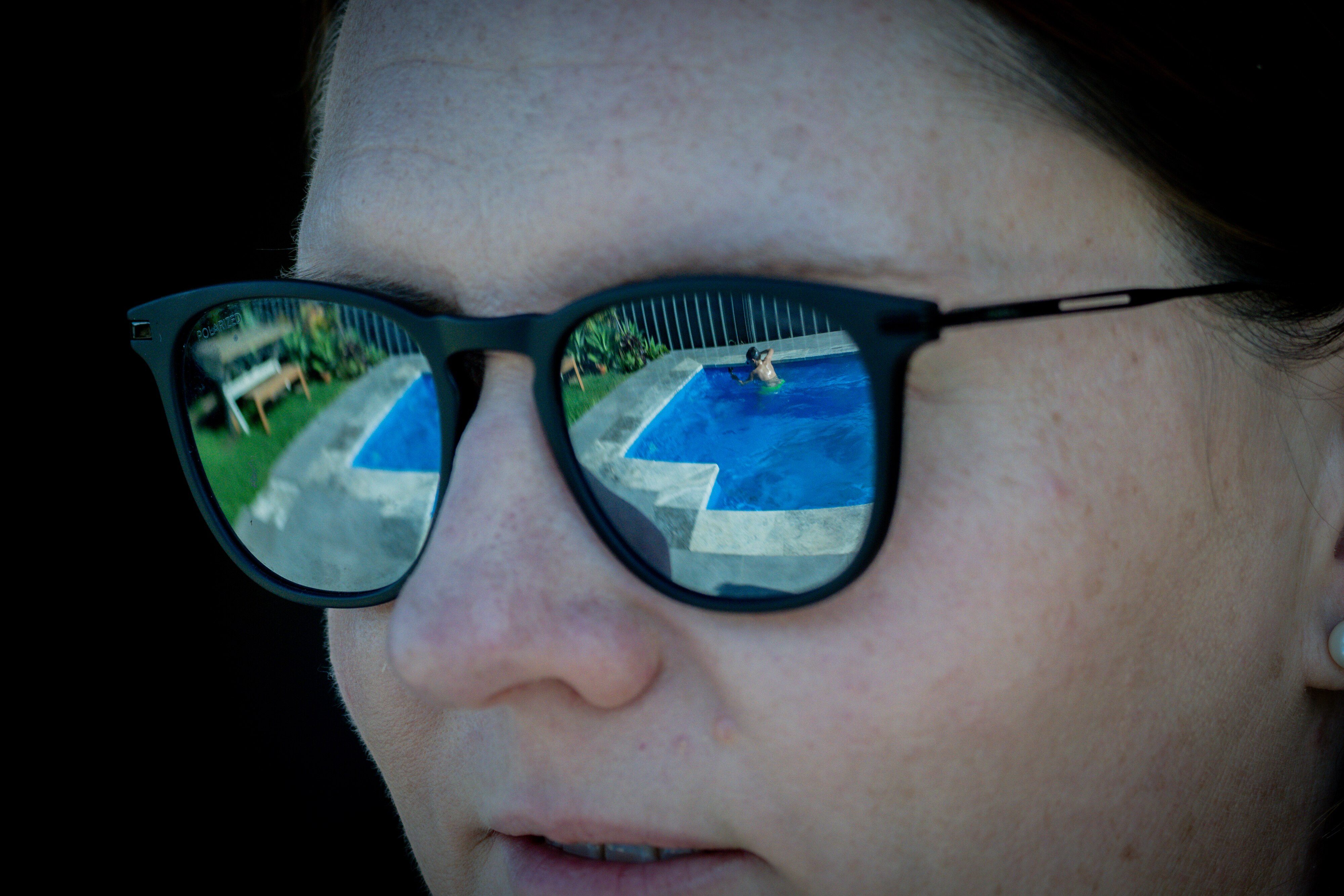 Jane's sunglasses reflecting her son playing in the pool.