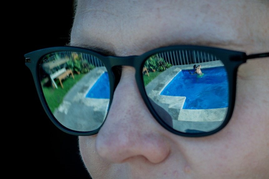 Jane's sunglasses reflecting her son playing in the pool.