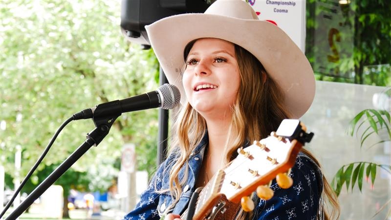 girl in cowgirl hat sings and plays guitar at busking festival