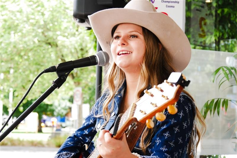 girl in cowgirl hat sings and plays guitar at busking festival