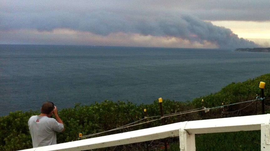 A man photographs a bushfire from the Strzelecki Lookout.