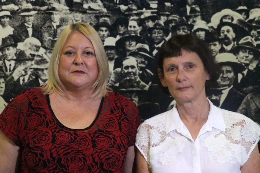 Tony Walkington and Pat Byrne standing in front of a large black and white photo of a group of people.