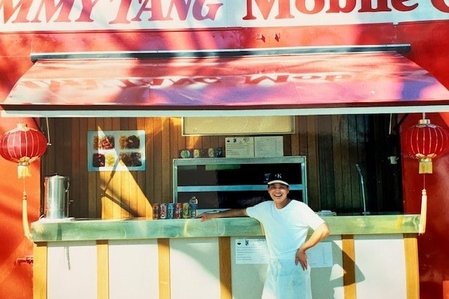A man smiling in front of a food truck.