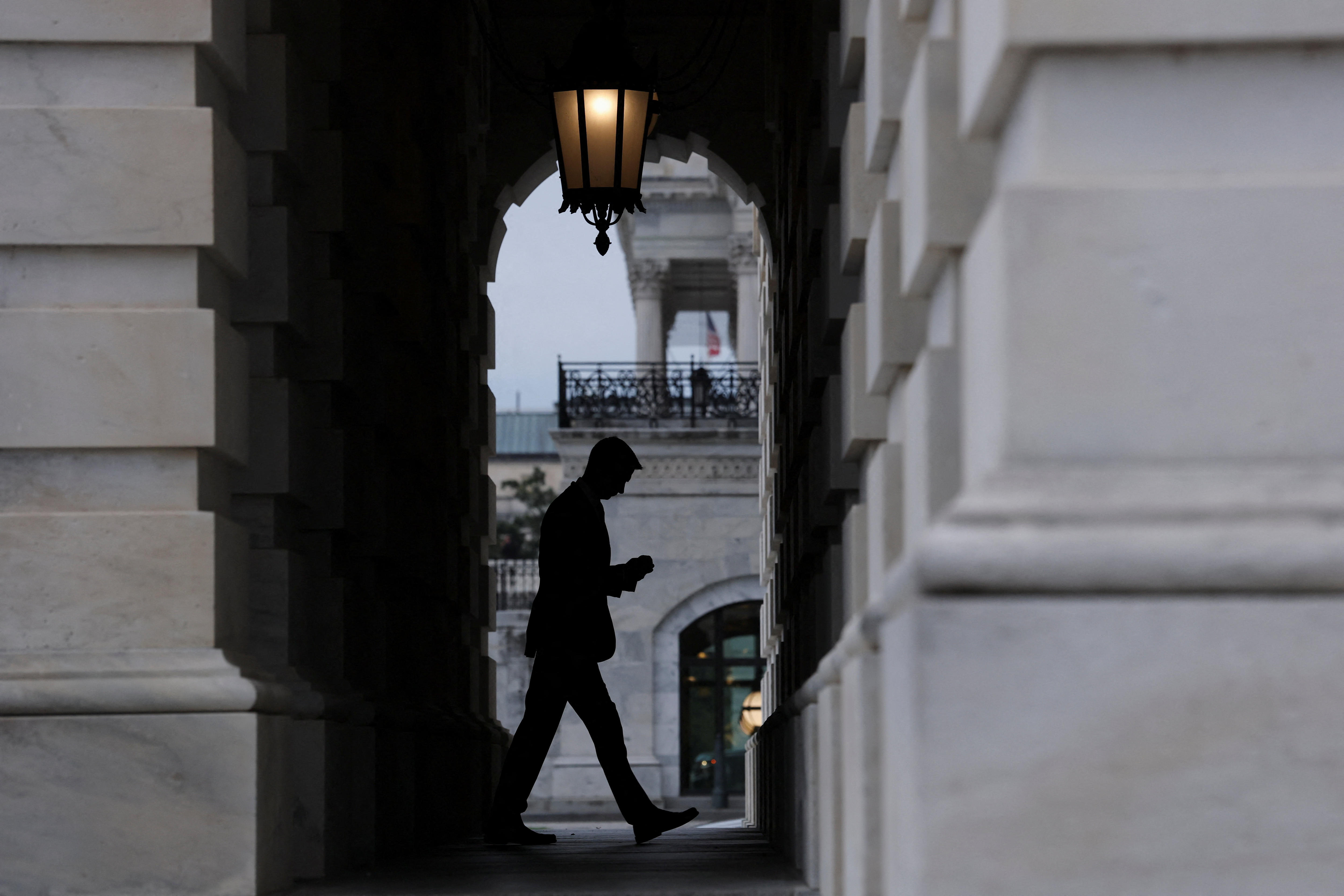 A man looks down at his phone as he walks past an archway.